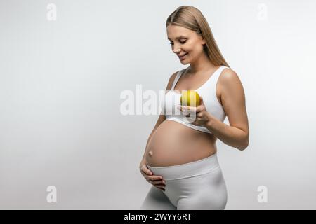 Lächelnde blonde schwangere Frau mit Apfel in den Händen Stockfoto