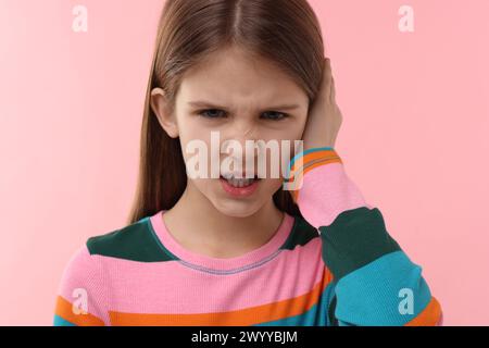 Hörprobleme. Kleines Mädchen, das an Ohrenschmerzen auf rosa Hintergrund leidet Stockfoto