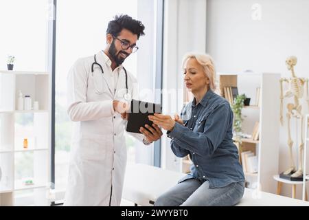 Erwachsener bärtiger Arzt, der Empfehlungen gibt und Tablette verwendet. Stockfoto