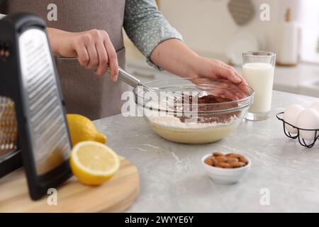 Frau macht Schokoladenteig mit Schneebesen in Schüssel an grauem Marmortisch, Nahaufnahme Stockfoto
