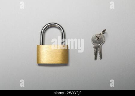Vorhängeschloss aus Stahl mit Schlüsseln auf grauem Hintergrund, Draufsicht Stockfoto