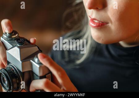 Eine Frau in einem schwarzen Kleid sitzt bequem und schätzt dabei eine klassische Kamera und fängt ihr Interesse an Fotografie in einem warmen Innenbereich bei Dämmerung ein. Stockfoto