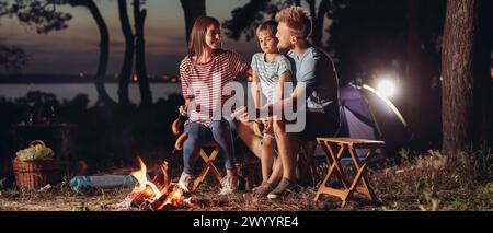 Familie braten Würstchen über dem Lagerfeuer am Abend Stockfoto