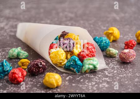 Papierkegel mit süßem bunten Popcorn auf dunklem Hintergrund Stockfoto