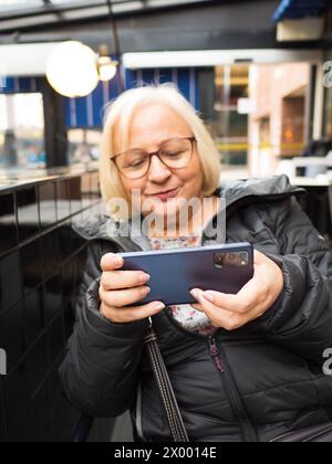 Unfokussierte blonde Gamer Großmutter liebt das Spielen auf dem Smartphone Stockfoto