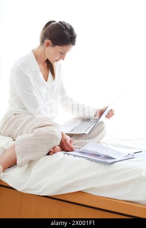 Frau, die auf dem Bett sitzt und einen Laptop benutzt. Stockfoto
