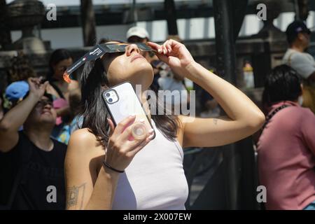 Eine Frau beobachtet die Sonnenfinsternis durch eine spezielle Sichtbrille während der Großen Nordamerikanischen Sonnenfinsternis. Große Menschenmassen versammeln den Angel de la Independencia, um eine teilweise Sonnenfinsternis zu erleben. Am 8. April 2024 in Mexiko-Stadt. (Foto: Ian Robles/ Credit: Eyepix Group/Alamy Live News Stockfoto