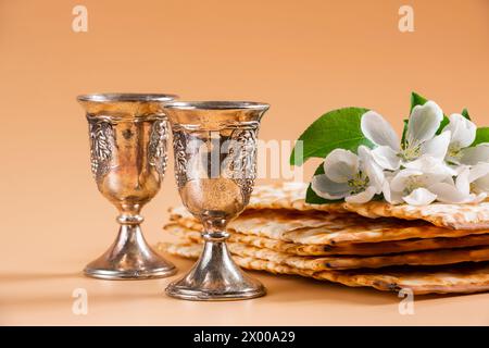 Alles Gute Zum Pessach. Traditioneller jüdischer Feiertag. Silberne Weinbecher, Frühlingsblumen und Matzobrot auf beigefarbenem Hintergrund. Kopierbereich. Stockfoto