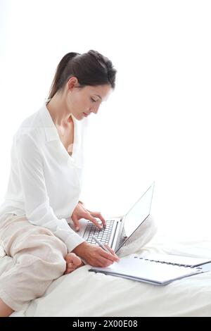 Frau, die auf dem Bett sitzt und einen Laptop benutzt. Stockfoto