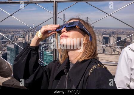 New York, Usa. April 2024. NEW YORK, NEW YORK – 08. APRIL: Eine Frau mit Schutzbrille sieht die partielle Sonnenfinsternis von der Aussichtsplattform im 86. Stock des Empire State Building am 8. April 2024 in New York City aus. Mit der ersten Sonnenfinsternis, die seit sieben Jahren Nordamerika durchquerte, war New York City nicht auf dem Weg der Totalität, da nur 90 % der Sonne vom Mond bedeckt waren; die nächste Sonnenfinsternis, die in den Vereinigten Staaten zu sehen ist, wird 2044 sein. Quelle: Ron Adar/Alamy Live News Stockfoto