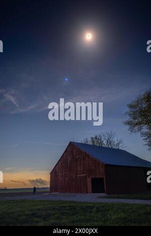 Die totale Sonnenfinsternis vom 8. April 2024, von Süd-Indiana aus gesehen. Zu sehen ist eine rote Scheune auf einer Landstraße während der Totalität. Rustikale ländliche Szene. Stockfoto