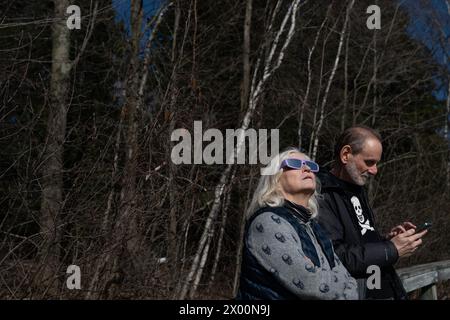 Granby, Kanada. April 2024. Eine Frau schaut durch ihre Sonnenbrille zur Sonnenfinsternis von 2024 in den Himmel, während ihr Mann ihre Fotos auf seinem Handy vor der Totalität überprüft. Quelle: Ben Nichols/Alamy Live News Stockfoto