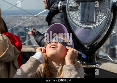 New York, Usa. April 2024. Die neunjährige Nika trägt eine Schutzbrille, um die partielle Sonnenfinsternis von der Aussichtsplattform im 86. Stock des Empire State Building am 8. April 2024 in New York City aus zu sehen. Mit der ersten Sonnenfinsternis, die seit sieben Jahren Nordamerika durchquerte, war New York City nicht auf dem Weg der Totalität, da nur 90 % der Sonne vom Mond bedeckt waren; die nächste Sonnenfinsternis, die in den Vereinigten Staaten zu sehen ist, wird 2044 sein. (Foto: Ron Adar/SOPA Images/SIPA USA) Credit: SIPA USA/Alamy Live News Stockfoto