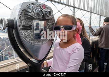 New York, Usa. April 2024. Die siebenjährige Sierra trägt eine Schutzbrille, um die partielle Sonnenfinsternis von der Aussichtsplattform im 86. Stock des Empire State Building am 8. April 2024 in New York City aus zu sehen. Mit der ersten Sonnenfinsternis, die seit sieben Jahren Nordamerika durchquerte, war New York City nicht auf dem Weg der Totalität, da nur 90 % der Sonne vom Mond bedeckt waren; die nächste Sonnenfinsternis, die in den Vereinigten Staaten zu sehen ist, wird 2044 sein. (Foto: Ron Adar/SOPA Images/SIPA USA) Credit: SIPA USA/Alamy Live News Stockfoto