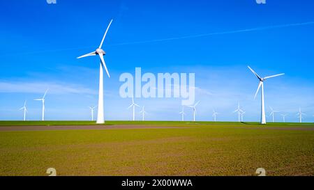 Eine Gruppe schlanker Windturbinen steht hoch in einem pulsierenden Feld in Flevoland und nutzt die Kraft des Windes an einem sonnigen Frühlingstag. Windkraftanlagen Stockfoto