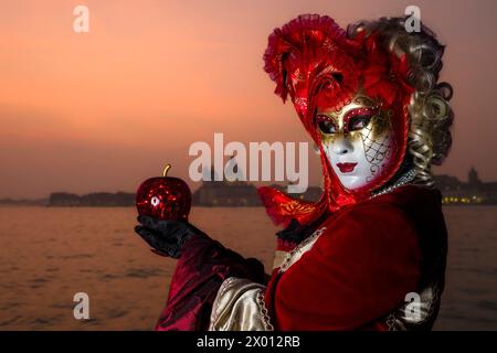 Porträt einer maskierten Frau in einem kreativen Kostüm, die auf der Insel San Giorgio di Maggiore posiert und den venezianischen Karneval bei Sonnenuntergang feiert. Stockfoto