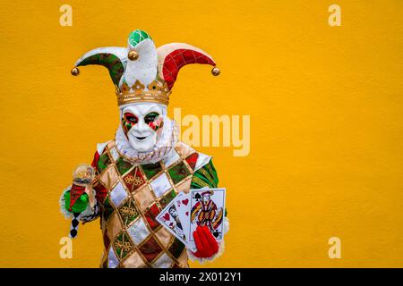 Porträt einer maskierten Person in einem kreativen Harlekin-Kostüm, posiert vor einer gelben Wand auf der Insel Burano, um das venezianische Karnev zu feiern Stockfoto