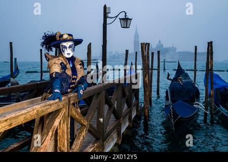 Porträt einer maskierten Frau in einem kreativen Kostüm, die auf dem Canale Grande posiert und den venezianischen Karneval feiert. Stockfoto