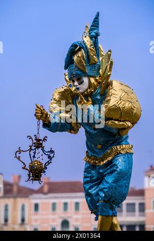 Eine maskierte Person in einem kreativen Harlekin-Kostüm, posiert auf dem Canale Grande, um den venezianischen Karneval zu feiern. Stockfoto