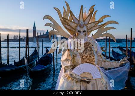 Porträt einer maskierten Frau in einem kreativen Kostüm, die auf dem Canale Grande posiert und den venezianischen Karneval feiert. Stockfoto