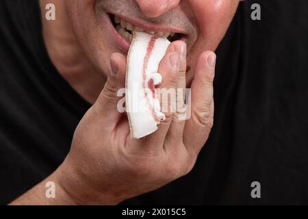 Ein Mann, dessen Gesicht nicht sichtbar ist, isst ein Stück Schmalz. Stockfoto