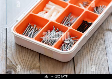 Sammlung von Nägeln, Daumennägeln, Schrauben, Kunststoff und Bolzen in Kunststoffkiste auf dem Holztisch Stockfoto