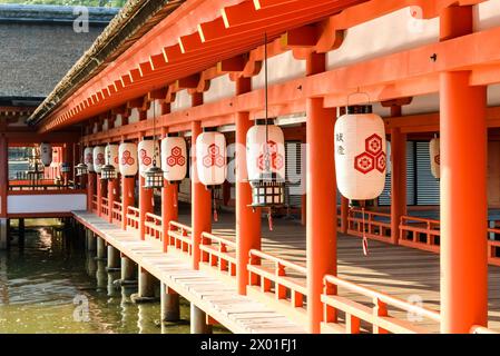 Laternen aus Papier und Messing hängen an den Holzvorsprüngen eines Gehwegs am Itsukushima Shinto-Schrein in Miyajima, Hiroshima, Japan. Stockfoto