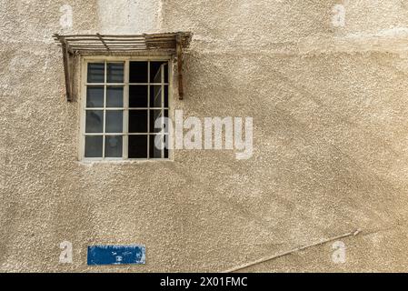 Ein offenes Fenster mit einem Schatten von der Sonne wirft Schatten entlang einer strukturierten Putzmauer in der Innenstadt einer Stadt im Nahen Osten. Stockfoto