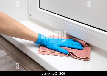 Die Hausfrau wischt die Plastikschwelle des Balkons mit einem Lappen ab. Nassreinigung der Wohnung. Hausfrau in Gummihandschuhen wäscht den Boden Stockfoto