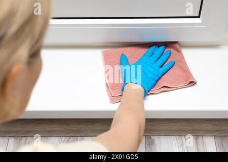 Die Hausfrau wischt die Plastikschwelle des Balkons mit einem Lappen ab. Nassreinigung der Wohnung. Hausfrau in Gummihandschuhen wäscht den Boden. Stockfoto