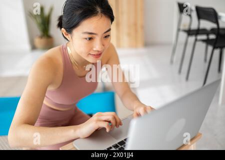 Junge asiatische Frau auf der Suche nach virtuellen Fitness-Klasse auf Laptop zu Hause Stockfoto