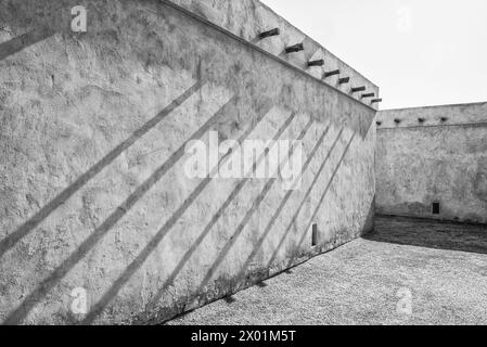 Schwarzweißbild einer Außenwand eines restaurierten traditionellen arabischen Hauses mit Sonnenlicht, das diagonale Schatten von Dachbalken wirft. Stockfoto