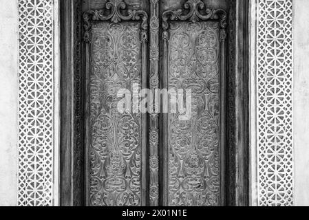 Einfarbige gefilterte Detailansicht einer aufwendig geschnitzten Außentür mit geschnitzten Gipsumrandungen eines restaurierten traditionellen arabischen Hauses. Stockfoto