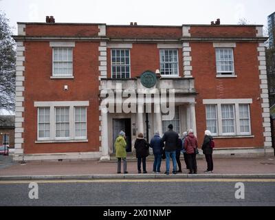 Touristen sehen das historische Gebäude der Port of London Authority (PLA) an der Hertsmere Road, West India Quay, London, Großbritannien. Das 1914 erbaute und im edwardianischen Barockstil gestaltete Gebäude aus rotem Backstein und Stein diente ursprünglich als zentraler Knotenpunkt für die Verwaltung der Londoner Docklands Stockfoto