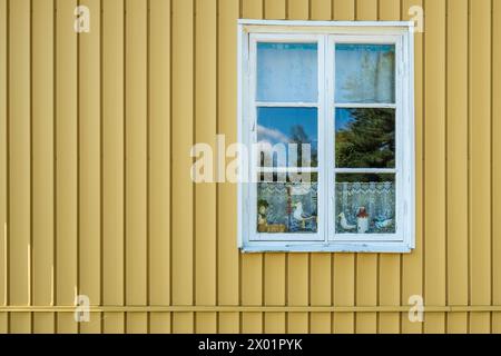 VAXHOLM, SCHWEDEN - 11. AUGUST 2018: Ein Fenster in der Wand eines traditionellen skandinavischen Hauses zeigt hölzerne geschnitzte Ornamente an einem Spitzenvorhang. Stockfoto