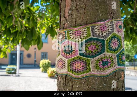 VAXHOLM, SCHWEDEN - 11. AUGUST 2018: Ein Baumstamm wird in ein Häkelband aus mehrfarbiger Wolle auf dem Platz einer skandinavischen Stadt gewickelt. Stockfoto