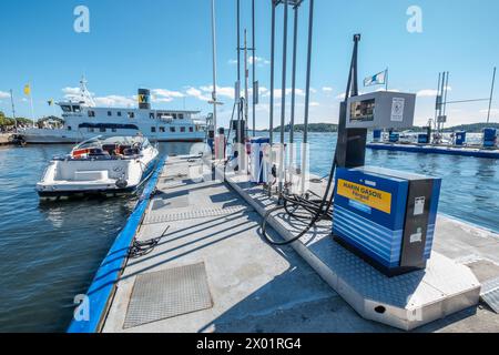 VAXHOLM, SCHWEDEN - 11. AUGUST 2018: Ein Motorboot, das an einer schwimmenden Tankstelle angedockt ist, bereitet sich an einem sonnigen Sommertag darauf vor, im Hafen Kraftstoff zu tanken. Stockfoto