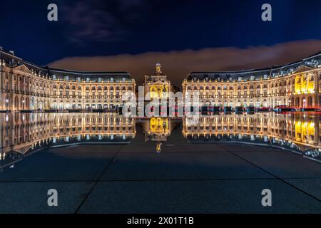 Entdecken Sie Bordeaux faszinierenden Nachtcharme auf diesem Langzeitfoto: Historisches Gebäude, das sich in ruhigem Wasser inmitten der Lichter der Stadt spiegelt. Stockfoto