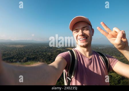 Glücklicher Mann, der Selfie vom Sommerferientag macht. Hübscher Tourist mit Mütze und einem Lächeln vor der Kamera vor tropischer Landschaft. Stockfoto