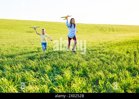 Ein Junge und ein Mädchen, die zwei gelbe und blaue Flugzeuge halten, spielen während des sonnigen Sommertages auf dem Feld Stockfoto