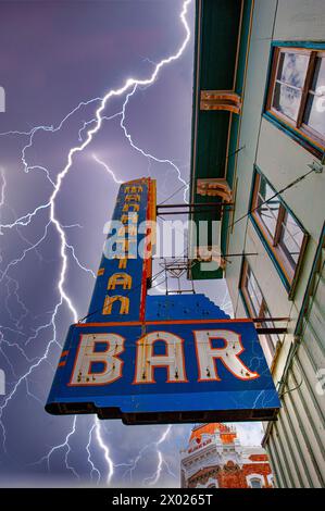 Ein eindrucksvolles Bild eines Retro-Bar-Schildes im Herzen von Colorado mit einem mächtigen Blitzschlag, der die unberechenbare Natur des Zorns in den Bergen einfängt Stockfoto
