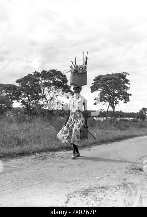 Eine junge Frau, die mit einem großen Einkaufskorb auf dem Kopf läuft. Nordrhodesien/Sambia um 1955 Stockfoto