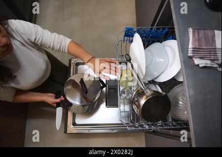 Blick von oben auf die Hausfrau, die einen Kochtopf aus Edelstahl herausnimmt und sauberes sterilisiertes Geschirr aus dem Geschirrspüler ausspült. Küchengeräte. Stockfoto