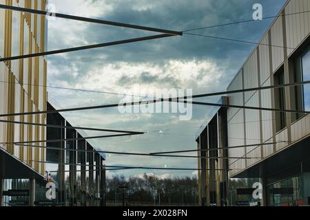 Moderne Architektur mit geometrischen Metallstrukturen vor einem dramatischen bewölkten Himmel, die zeitgenössisches urbanes Design und offene Räume präsentiert. Stockfoto