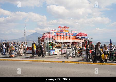 Menschen gehen entlang der Uferpromenade, Kiosk an der Via Partenope, Vesuv im Hintergrund, Neapel, Italien. Stockfoto