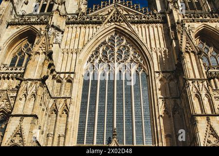 Gotische Architektur an der Fassade einer Kathedrale, mit einem großen Buntglasfenster und kunstvollen Steinschnitzereien unter klarem Himmel in York, Nord Stockfoto