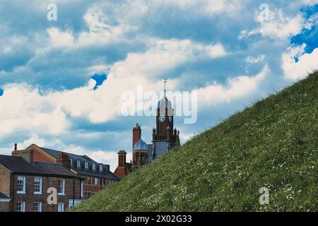 Malerische europäische Stadt mit historischen Gebäuden und einem Uhrenturm vor einem lebendigen blauen Himmel mit flauschigen Wolken und einem üppigen grünen Hügel im Vorfeld Stockfoto