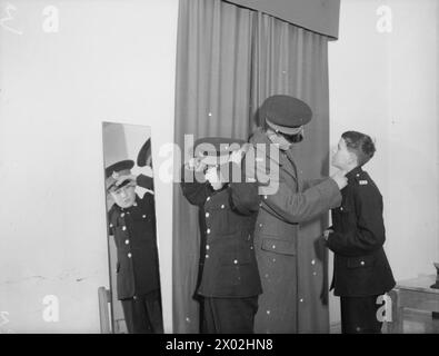 DER 14-JÄHRIGE JUNGE IST MITGLIED DER ROYAL MARINES BAND. 8. JANUAR 1942, SCARBOROUGH. DER 14-JÄHRIGE REGINALD DAVID WARDEN TRAT DER ROYAL MARINE SCHOOL OF MUSIC IN SCARBOROUGH BEI UND WURDE IHR JÜNGSTES MITGLIED. DIE SCHULE VERSORGT ALLE MUSIKER UND MARINEBANDS MIT HM-SCHIFFEN UND LANDBASEN. - Reginald mag ein kleiner Junge sein, aber sie haben eine Uniform für ihn, hier passt er seine Mütze, nachdem er seine Uniform angezogen hat Stockfoto