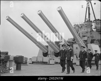 DIE ROYAL NAVY WÄHREND DES ZWEITEN WELTKRIEGS - HM King George VI mit Captain C H L Woodhouse (links), und Admiral Sir John Tovey (rechts), Oberbefehlshaber der Home Fleet, spaziert unter den vier 14-Zoll-Geschützen des Y-Turms an Bord des Schlachtschiffs HMS HOWE während eines Besuchs der Home Fleet in Scapa Flow George VI, King, Tovey, John Cronyn, Woodhouse, Charles Henry Lawrence, Royal Navy, HOWE (HMS) Stockfoto