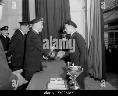 FIFTH SEA LORD VERLEIHT AUSZUBILDENDEN AUS DER FLOTTE PREISE. 15. UND 16. DEZEMBER 1943, ROYAL MARINEFLUGSTRAININGS, NEWCASTLE-UNDER-LYME. DER FÜNFTE SEA LORD UND CHEF DER MARINEFLUGAUSRÜSTUNG, KONTERADMIRAL D W BOYD, CBE, DSC, ÜBERREICHTE PREISE FÜR DIE AUSSCHEIDUNGSZEIT DER FLOTTENLUFTWAFFENAUSZUBILDENDEN BEI DER R N A T E - DER FÜNFTE SEA LORD ÜBERREICHTE DEM BESTEN VERLIERER SEINEN EIGENEN POKAL. der 17-jährige Lehrling P E Tucker aus Shoeburyness, Kent, der so gut kämpfte, obwohl er seinen Boxkampf um Punkte verlor Stockfoto